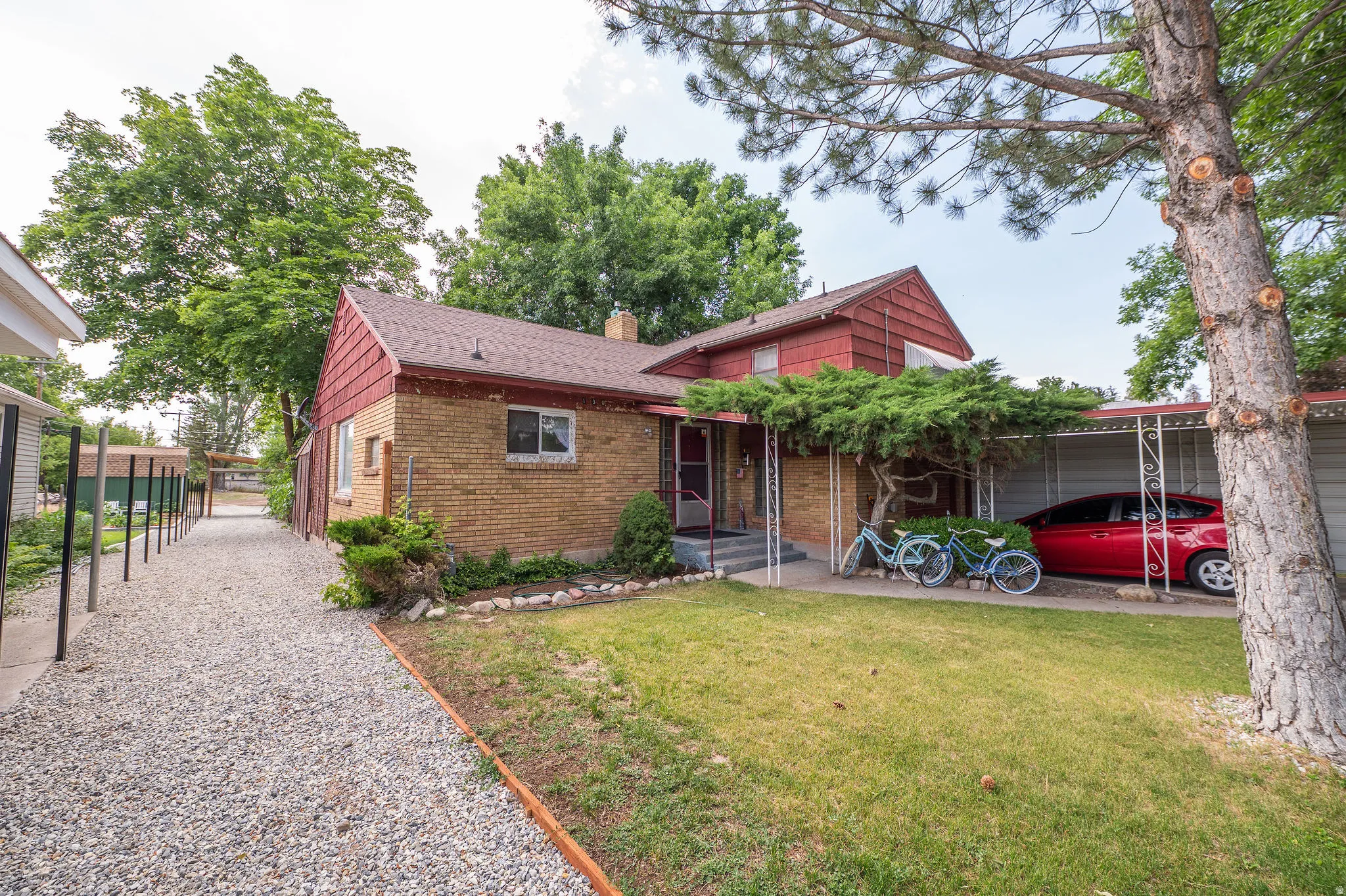 Brick exterior with a red shingle roof, complemented by a covered carport and a gravel side path