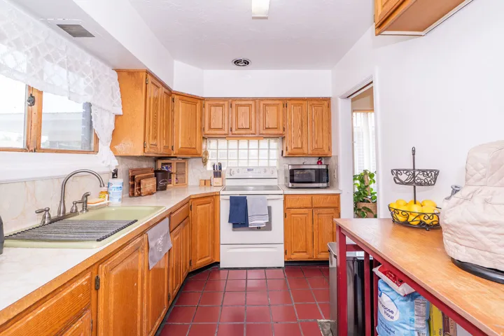 Kitchen featuring wood cabinetry, white countertops, tile flooring, a window above the sink, and a white electric range