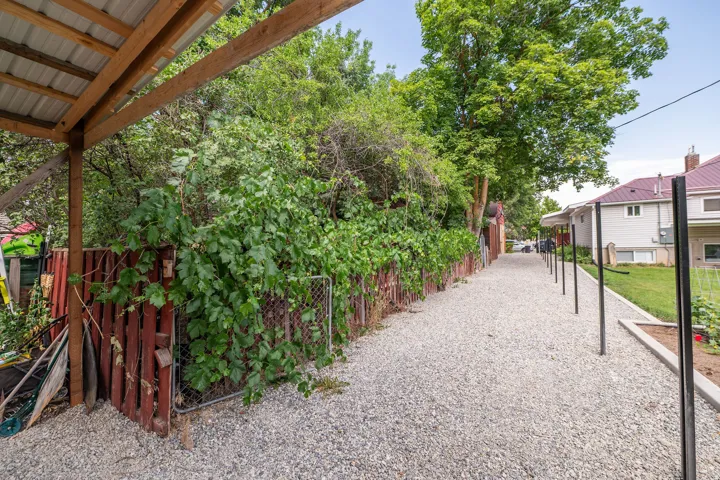 Gravel pathway bordered by a wooden fence with lush greenery and a covered structure