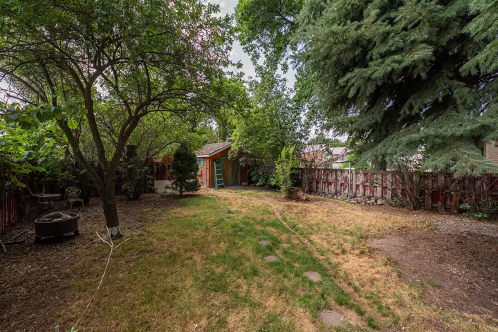 Expansive backyard featuring mature trees, a detached storage shed with a red exterior and green trim, a wooden perimeter fence, and stepping stones