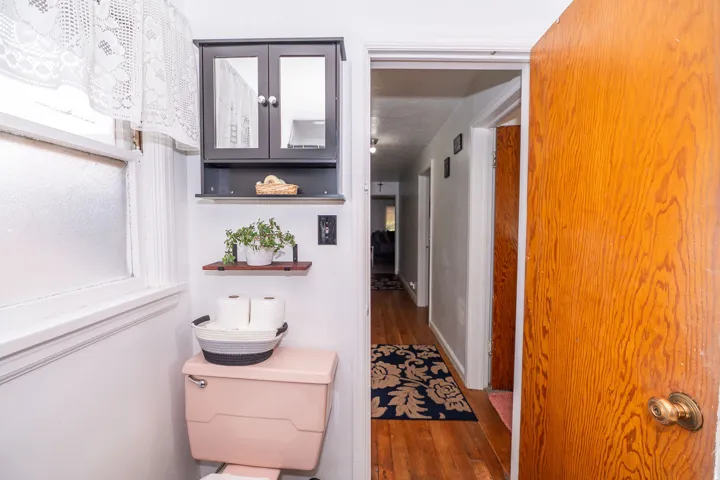 Compact bathroom featuring a window with privacy glass, a wall-mounted storage cabinet with mirrored doors, a floating shelf, and a light-colored toilet