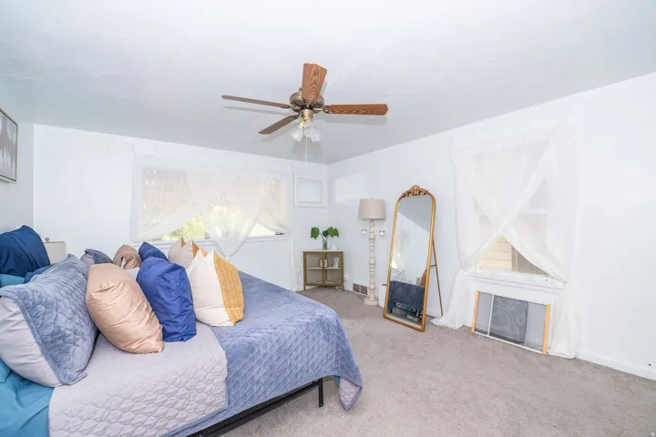 Spacious room featuring neutral carpet flooring, white walls, two windows, and a ceiling fan