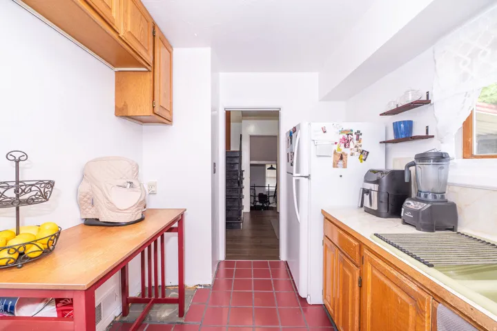 Kitchen featuring warm wood cabinetry, neutral countertops, and red tile flooring