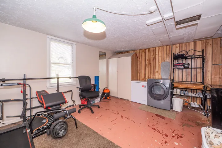 Lower-level area featuring a window, painted concrete flooring, wood paneling, and utility hookups