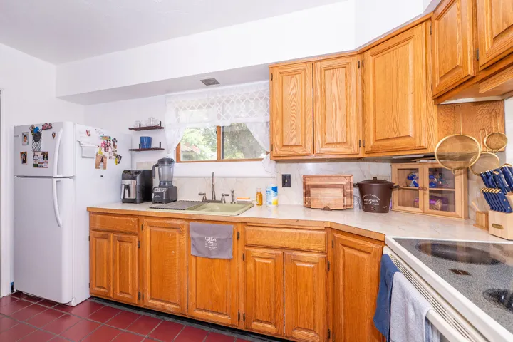 Kitchen featuring wood cabinetry, solid surface countertops, white appliances, and a window with natural light