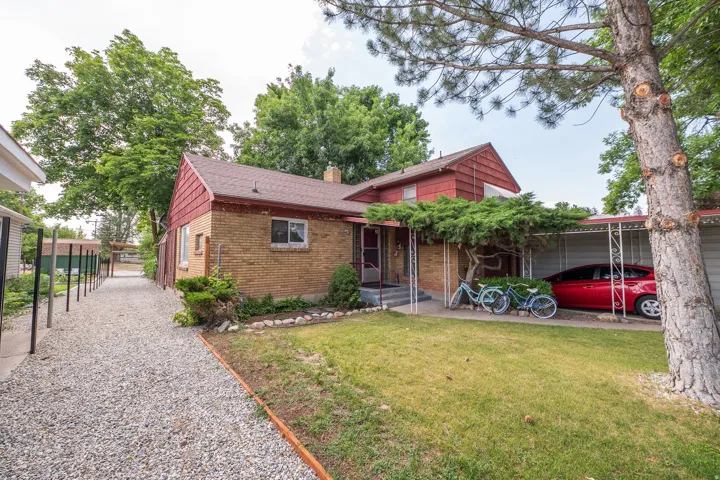 Brick exterior with a red shingle roof, complemented by a covered carport and a gravel side path