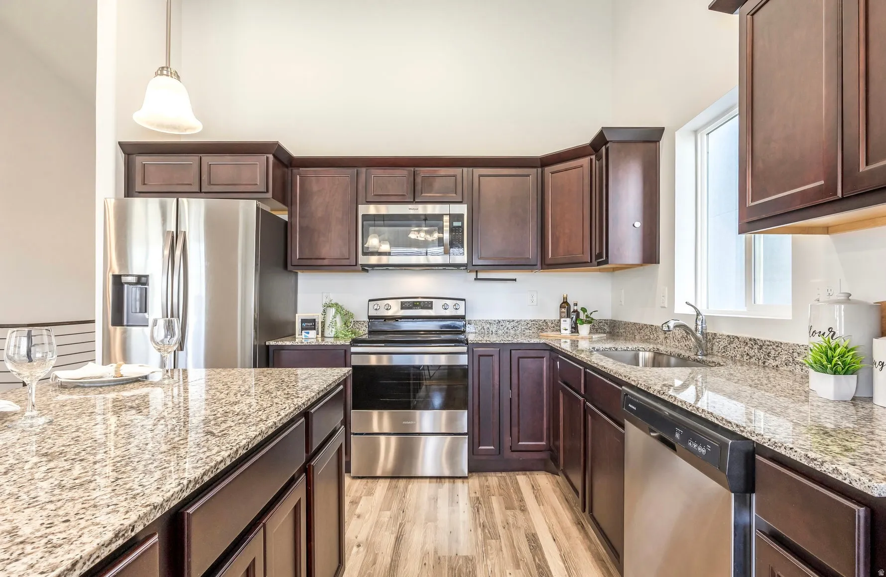 Modern kitchen featuring stainless steel appliances, rich wood cabinetry, stone countertops, wood-finish flooring, and a single window for natural light