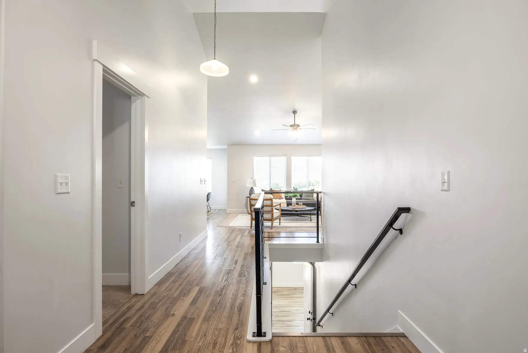 Upper-level hallway featuring wood-finish flooring, a modern white pendant light fixture, recessed lighting, and a contemporary black metal stair railing