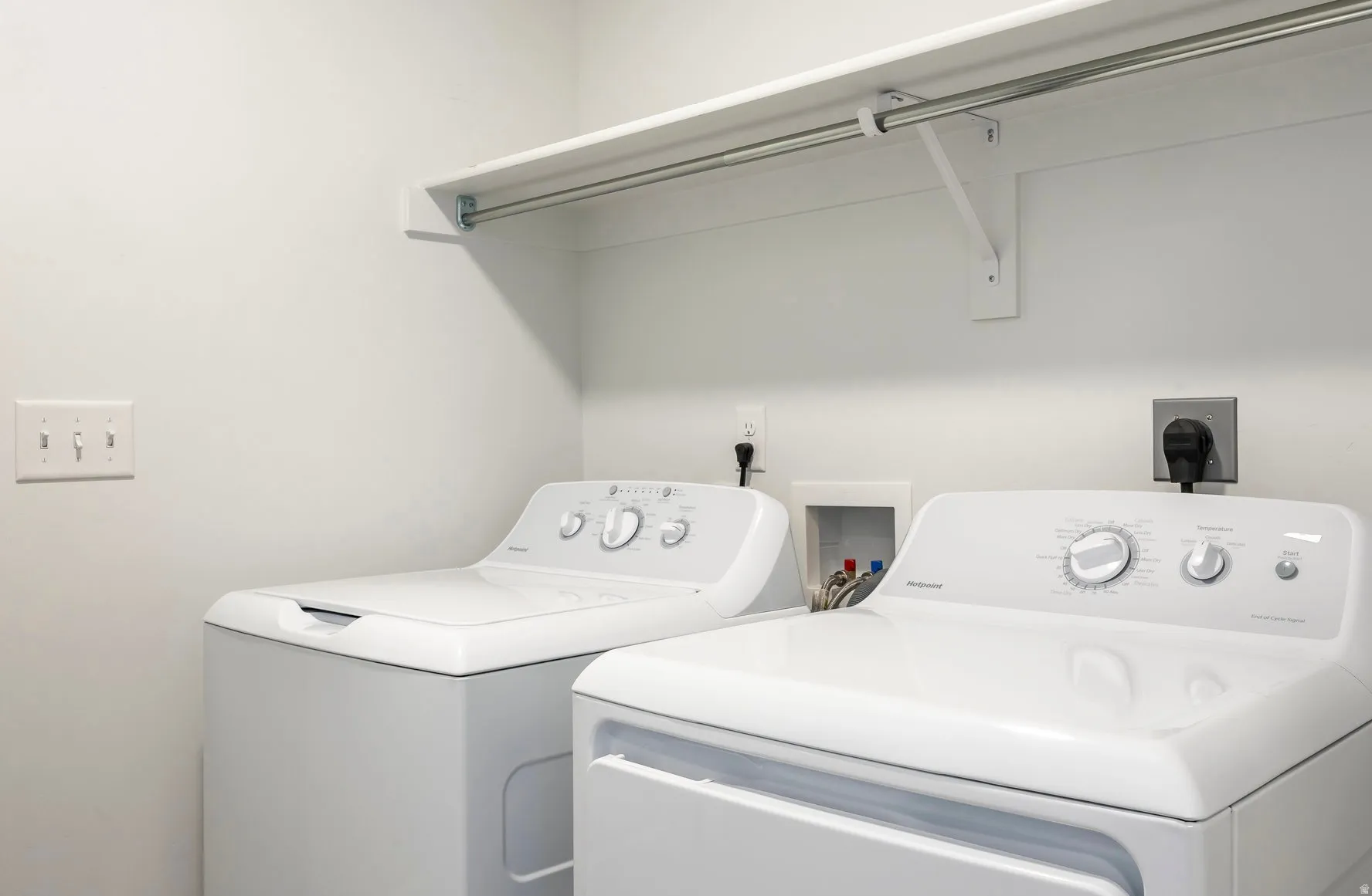 Dedicated laundry area featuring a white built-in shelving unit with a hanging rod, light-toned wall paint, and electrical outlets