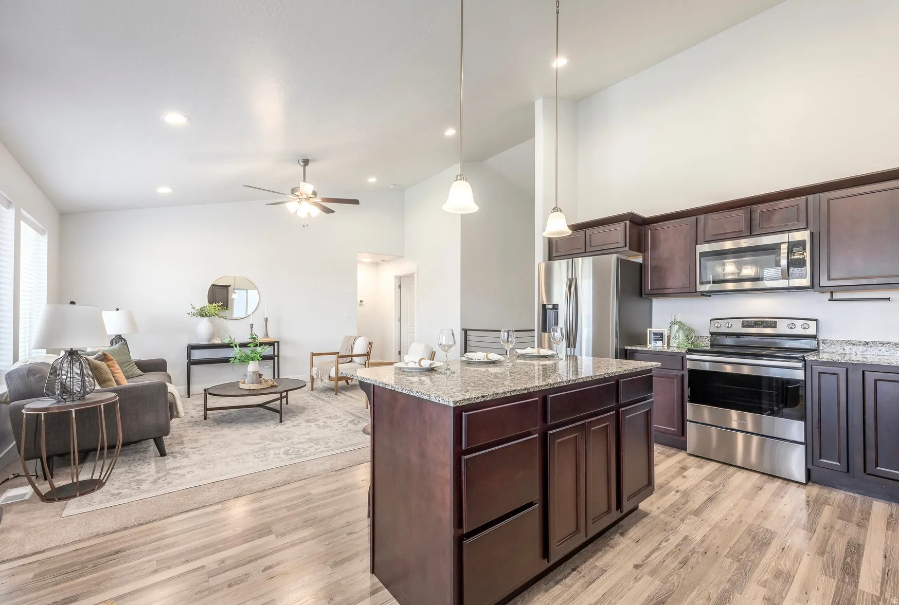 Open-concept living space featuring a kitchen island with pendant lighting, wood-finish flooring, dark wood cabinetry, stainless steel appliances, and high ceilings
