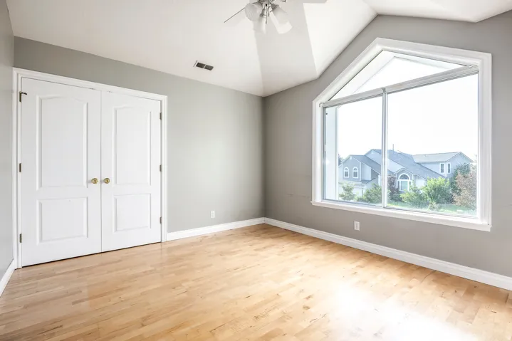 Expansive room featuring light wood-finish flooring, a vaulted ceiling, and a large angled picture window