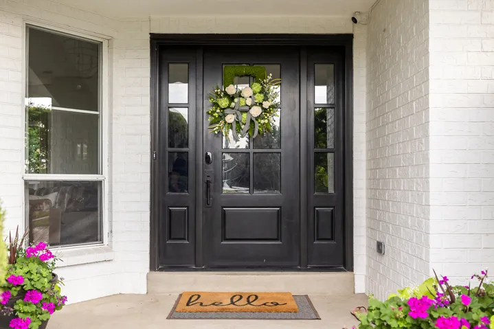 White painted brick exterior featuring a black paneled entry door with sidelights