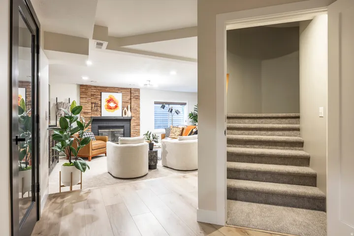 Finished lower level featuring a stacked stone fireplace with a black mantel, wood-finish flooring, recessed lighting, and a carpeted staircase
