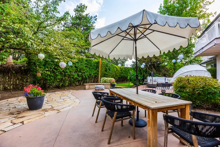 Expansive outdoor living area featuring a light-toned wood dining table with an umbrella, a stamped concrete patio, and a natural stone pathway