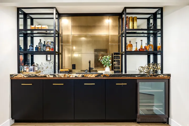 Built-in wet bar featuring a dark stone countertop, undermount sink with a matte black faucet, and a brass-toned textured backsplash