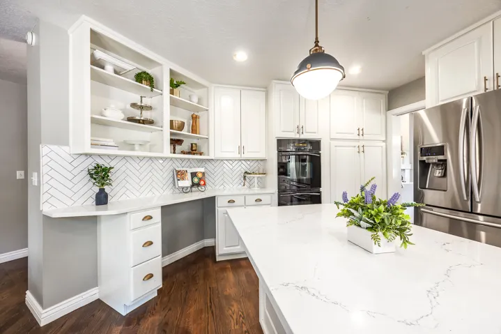 Bright kitchen featuring white cabinetry, a large center island with a stone-finish countertop, herringbone tile backsplash, and built-in stainless steel appliances