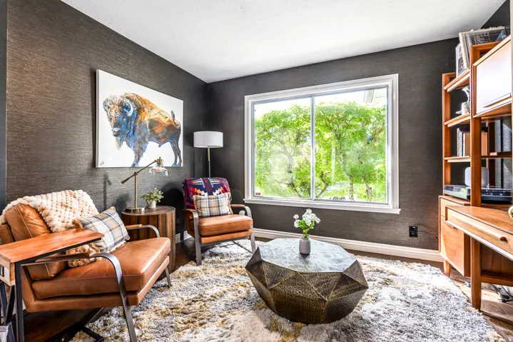 Room featuring textured dark wall coverings, a large window with white trim, and light wood-finish flooring