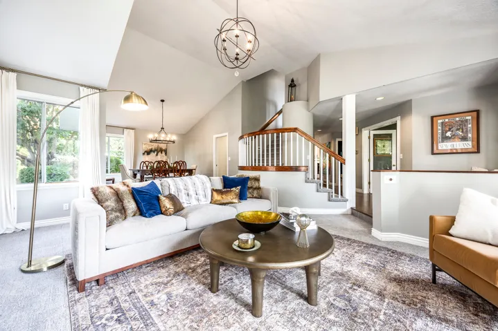 Vaulted ceiling living space with a dining area, featuring a staircase with wood-finish handrails and white balusters