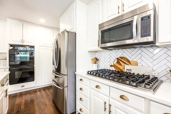 Kitchen featuring bright white cabinetry, stainless steel appliances, a five-burner gas cooktop, and a white herringbone tile backsplash