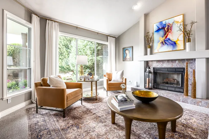 Spacious living area featuring a stone fireplace with a white mantel, large picture windows, vaulted ceiling, and recessed lighting