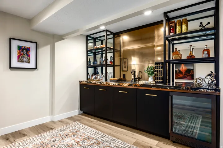 Wet bar featuring dark cabinetry with gold-toned hardware, a stone countertop, and an integrated beverage refrigerator