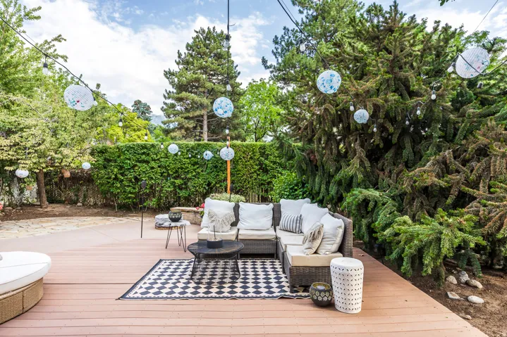 Expansive outdoor deck area featuring composite decking, string lights, and mature perimeter greenery