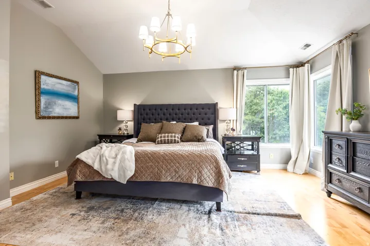 Vaulted ceiling with an elegant chandelier, wood-finish flooring, and large windows providing abundant natural light