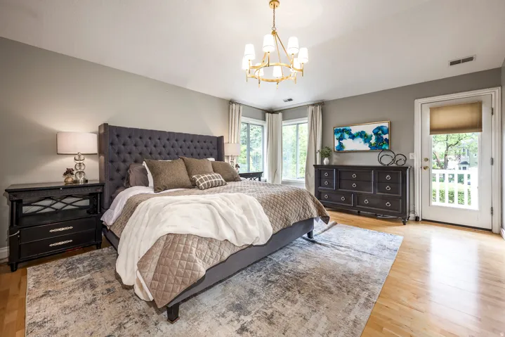 Bedroom with light wood-finish flooring, a wall-mounted brass chandelier, and light gray walls