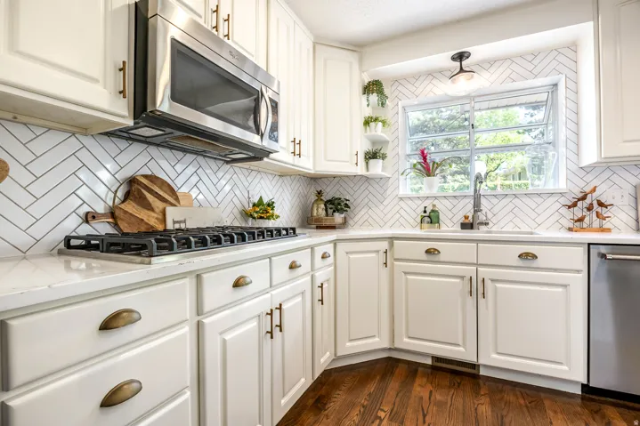 Kitchen featuring white shaker-style cabinetry, a white herringbone tile backsplash, and light-toned countertops