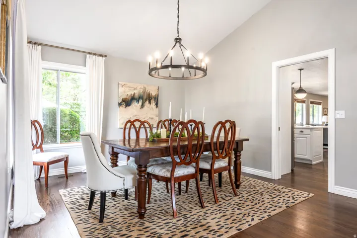 Vaulted ceiling dining room featuring wood-finish flooring, a large window, and a circular iron chandelier