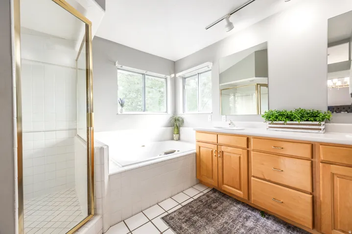 Bathroom featuring a spacious soaking tub, separate glass-enclosed shower, dual vanity with wood cabinetry, rectangular mirrors, and track lighting