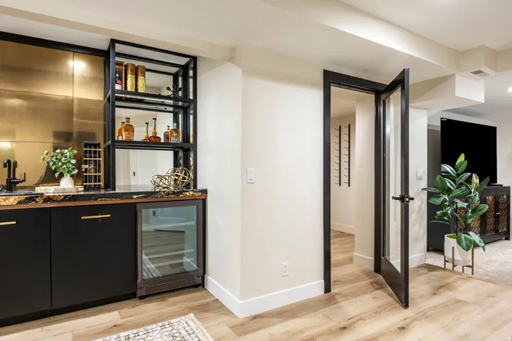 Wet bar featuring black cabinetry, a dark countertop, a built-in beverage refrigerator, and a gold-toned backsplash