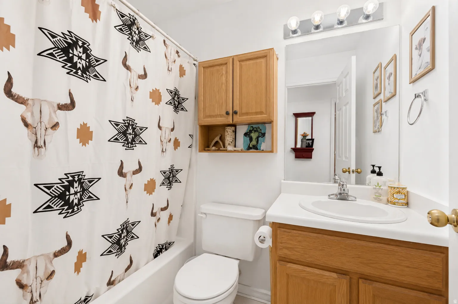 White bathroom featuring a built-in tub with shower, a single vanity with an integrated sink, and an oak-finish cabinet with open shelving