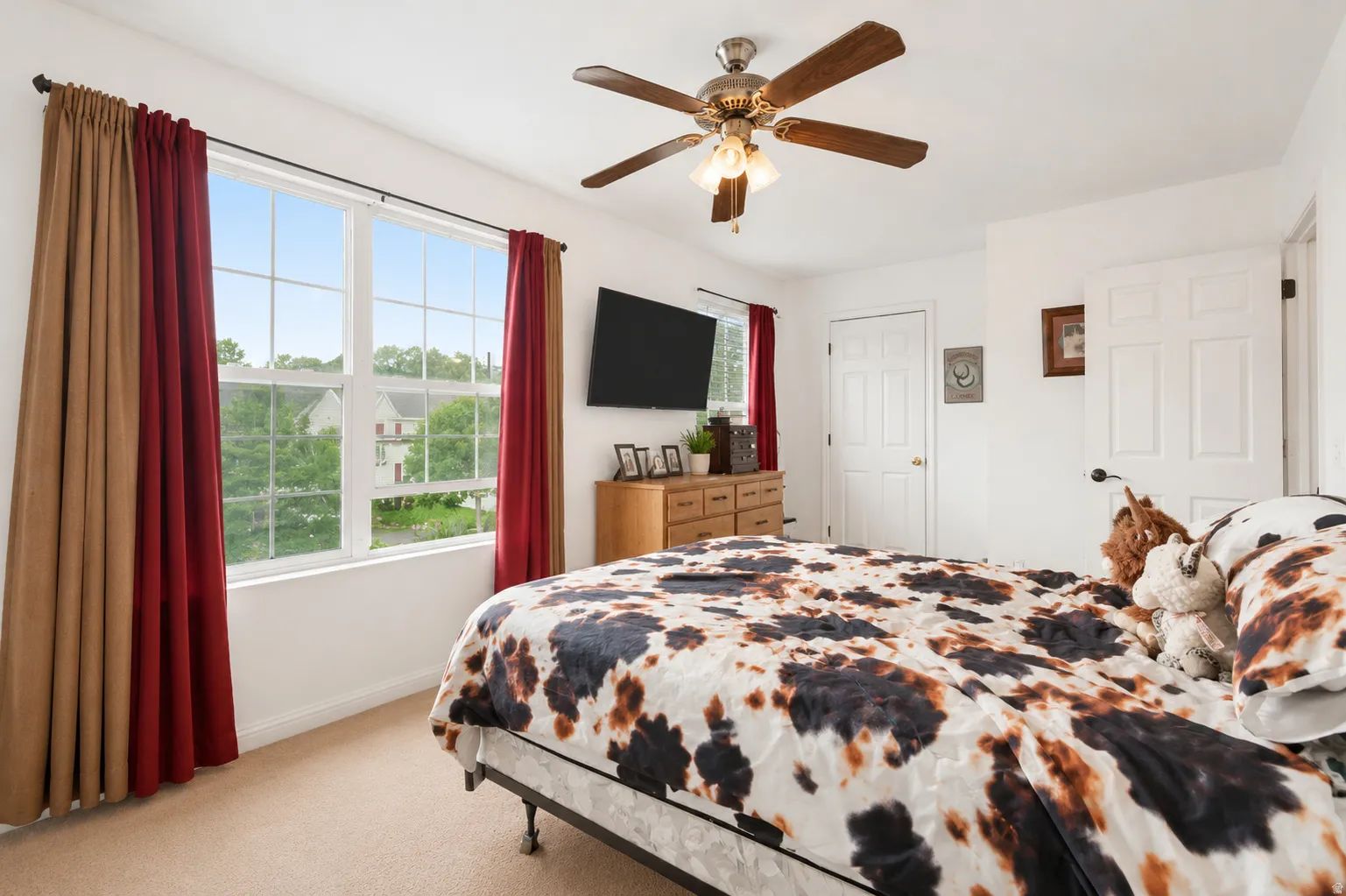 Bedroom featuring a large window, a ceiling fan with integrated lighting, and two white panel doors