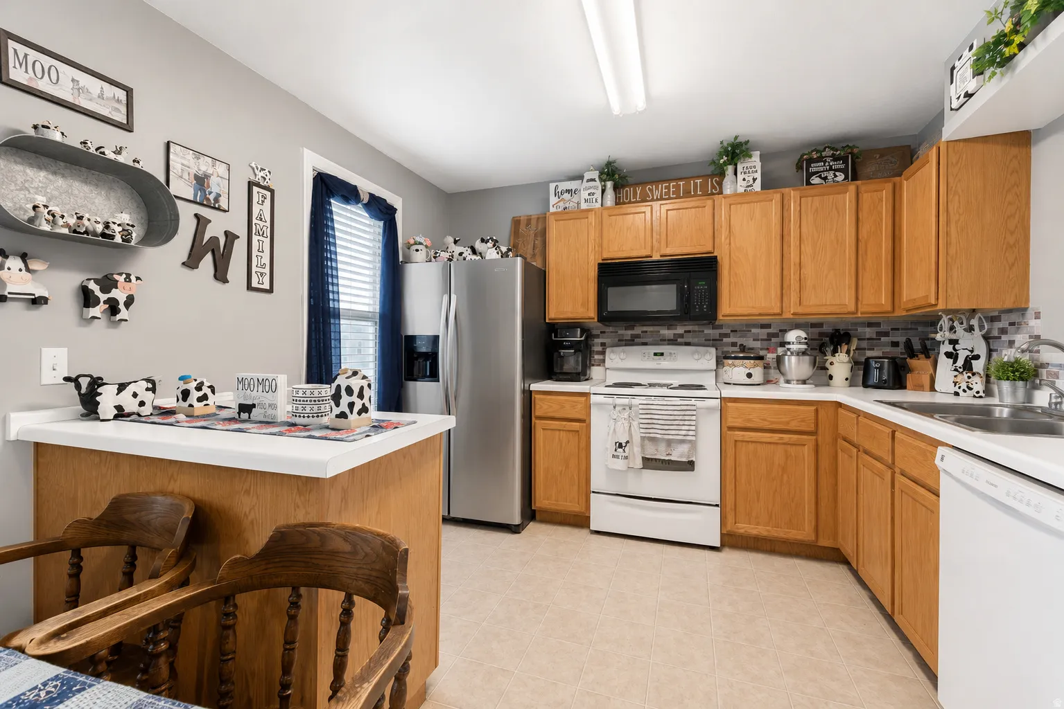 Well-appointed kitchen featuring wood cabinetry, white countertops, stainless steel refrigerator, white range, and a tiled backsplash