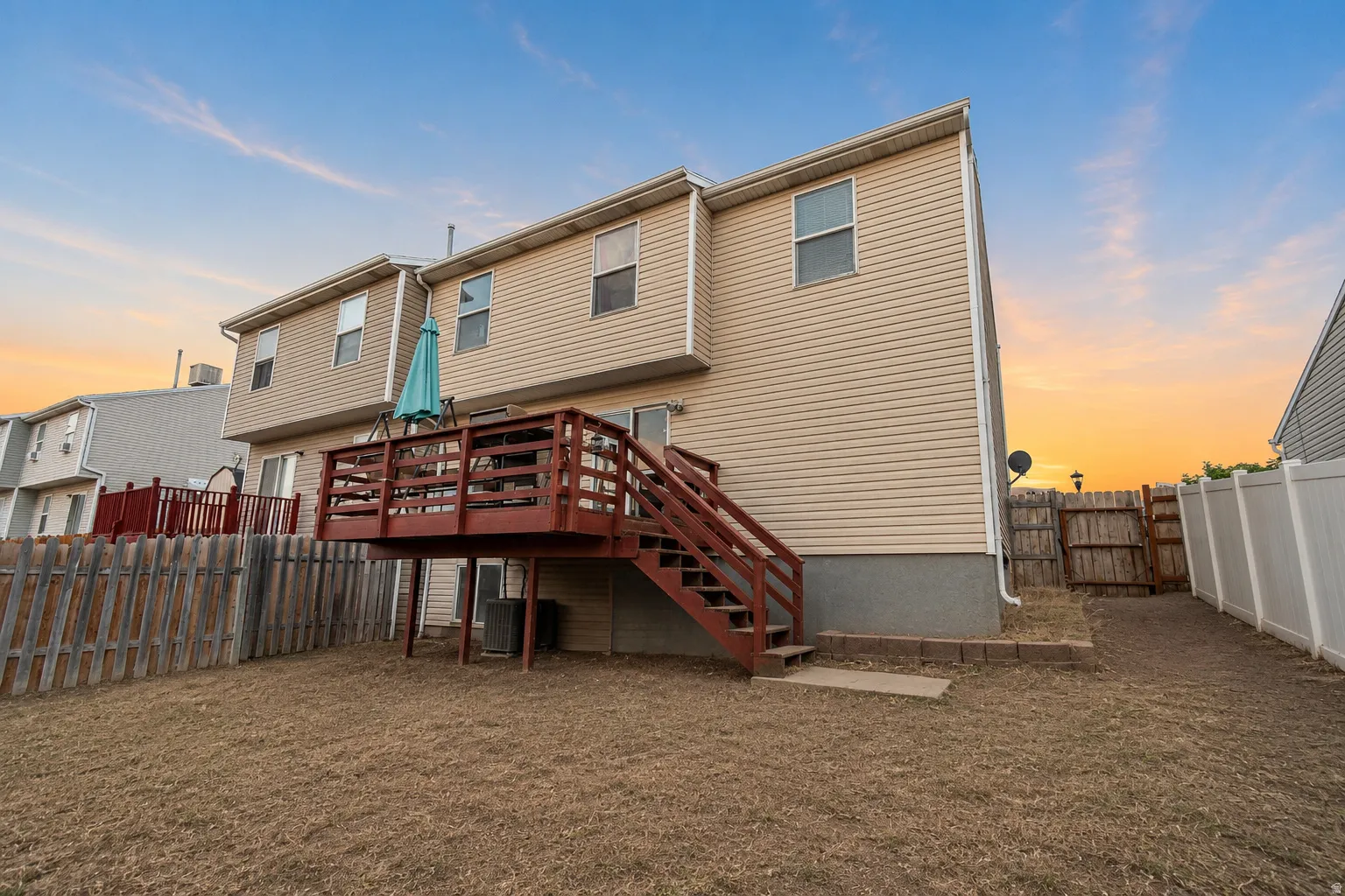 Rear exterior featuring a spacious elevated wood deck with stairs, beige horizontal siding, and multiple windows