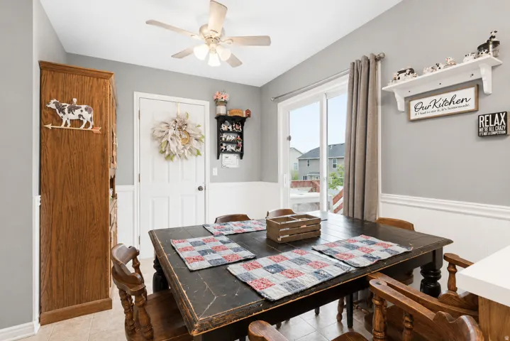 Dining area featuring a painted ceiling fan, light gray walls with white wainscoting, and tile flooring