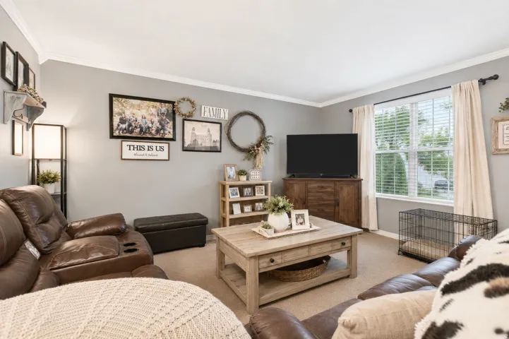 Living area featuring neutral wall paint, crown molding, a large window with blinds and drapes, and recessed lighting