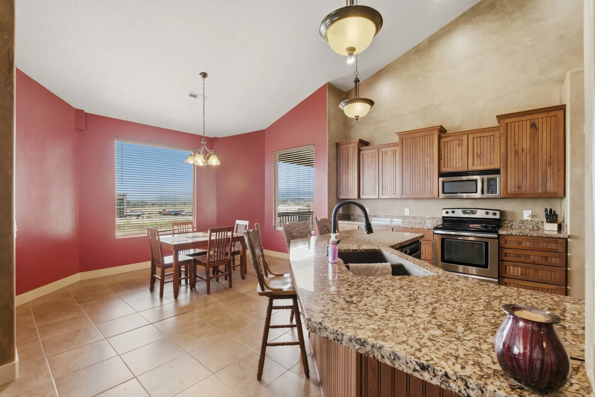 Kitchen featuring a granite-topped island with an undermount sink, wood cabinetry, stainless steel appliances, and tile flooring