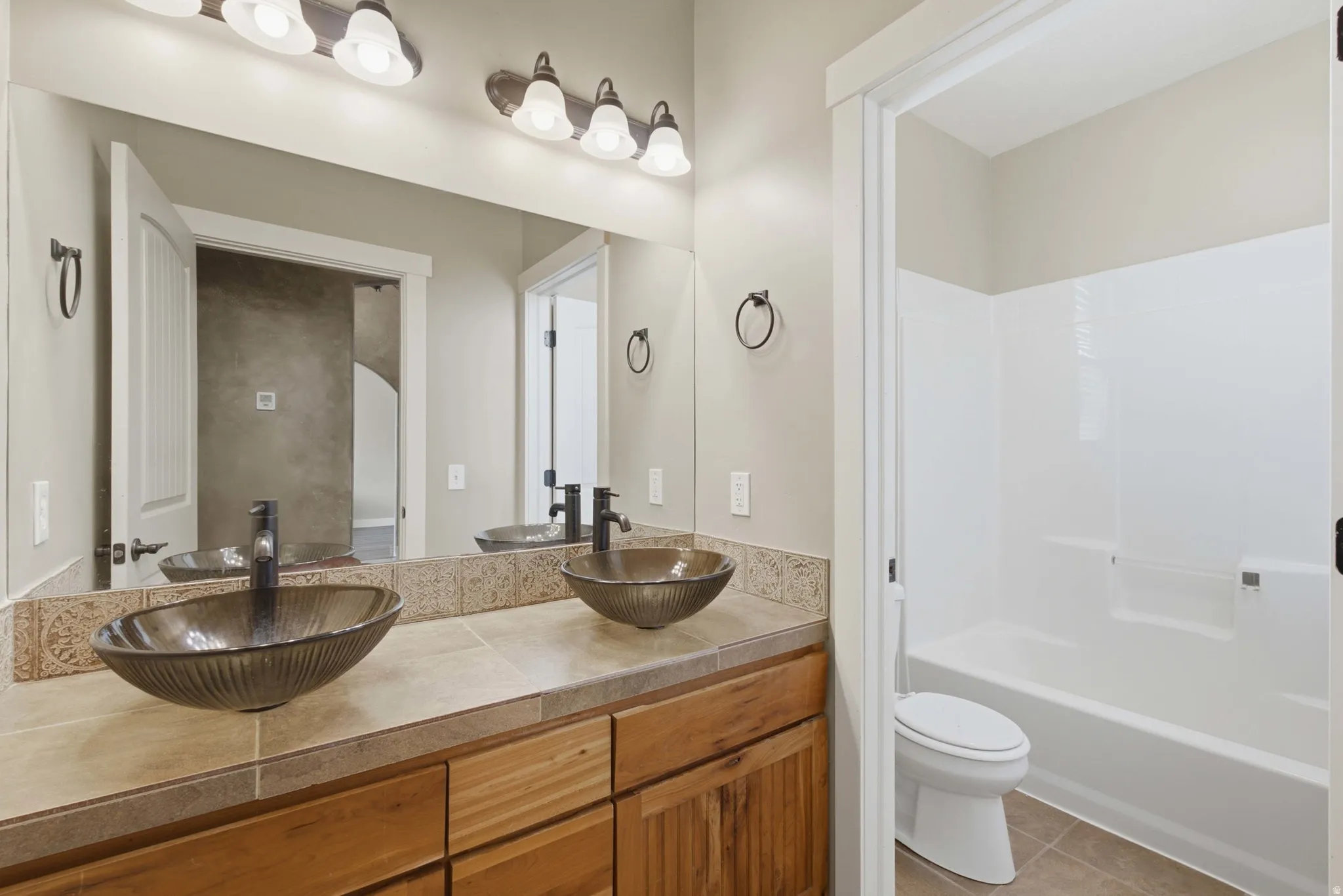 Double vanity featuring vessel sinks with dark bronze fixtures, tile countertops, and wood-finish cabinetry