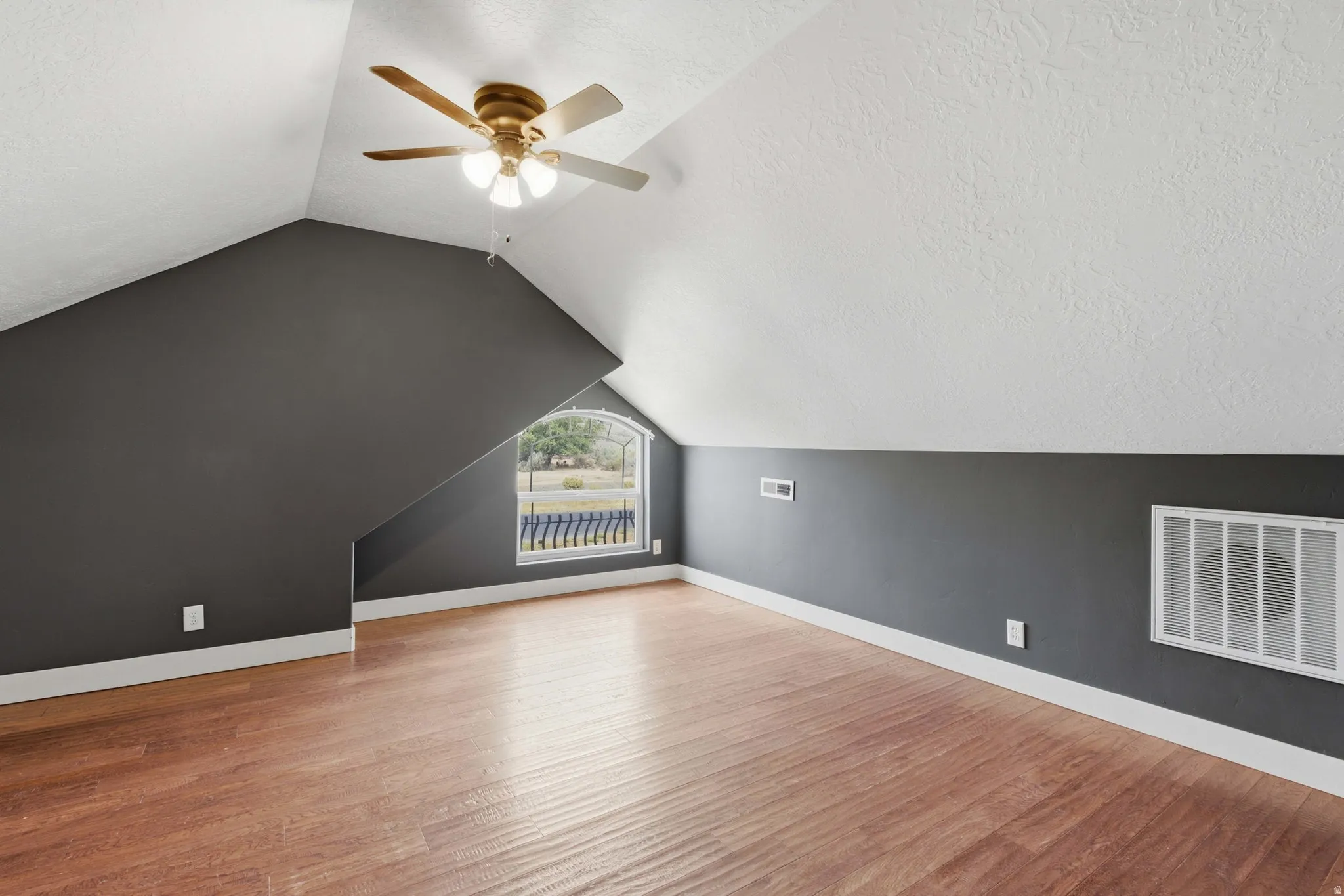 Sloped ceiling room featuring wood-finish flooring, a ceiling fan, and an arched window