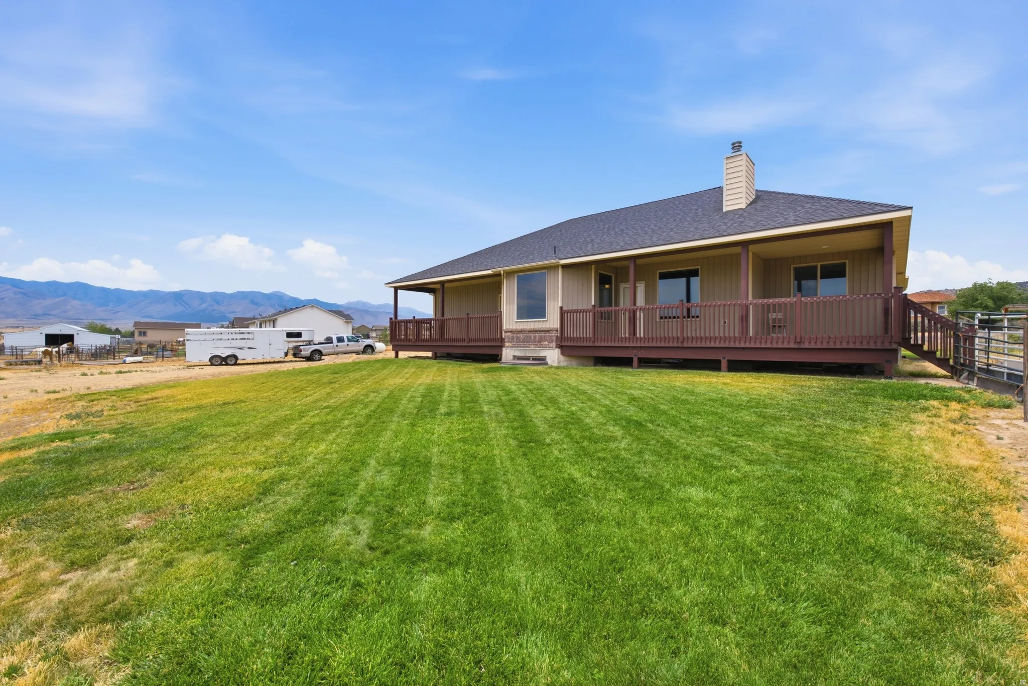 Expansive green lawn with a tan exterior residence featuring a covered deck, dark brown railing, and an exterior chimney
