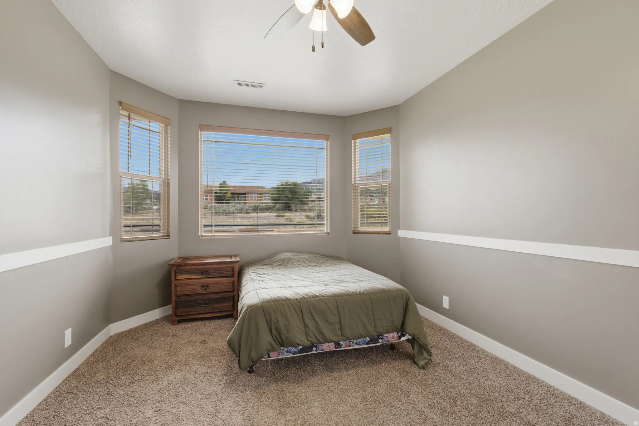 Carpeted room featuring multiple windows with blinds, a ceiling fan, and baseboard trim