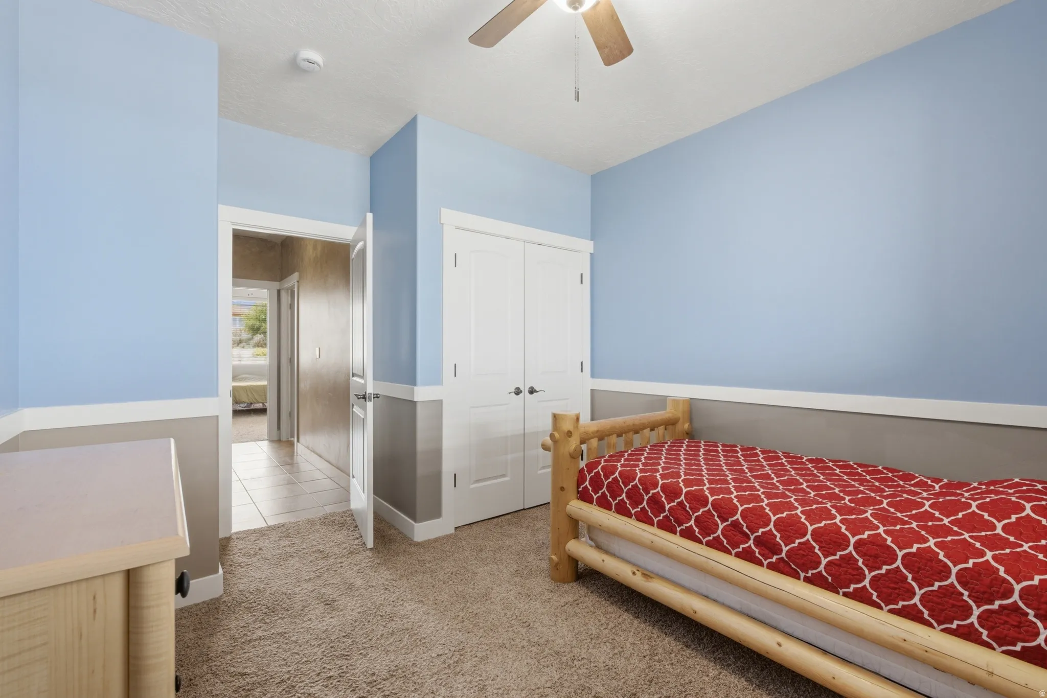 Carpeted room with a two-tone wall treatment, featuring a ceiling fan with light fixture and a built-in closet with double doors