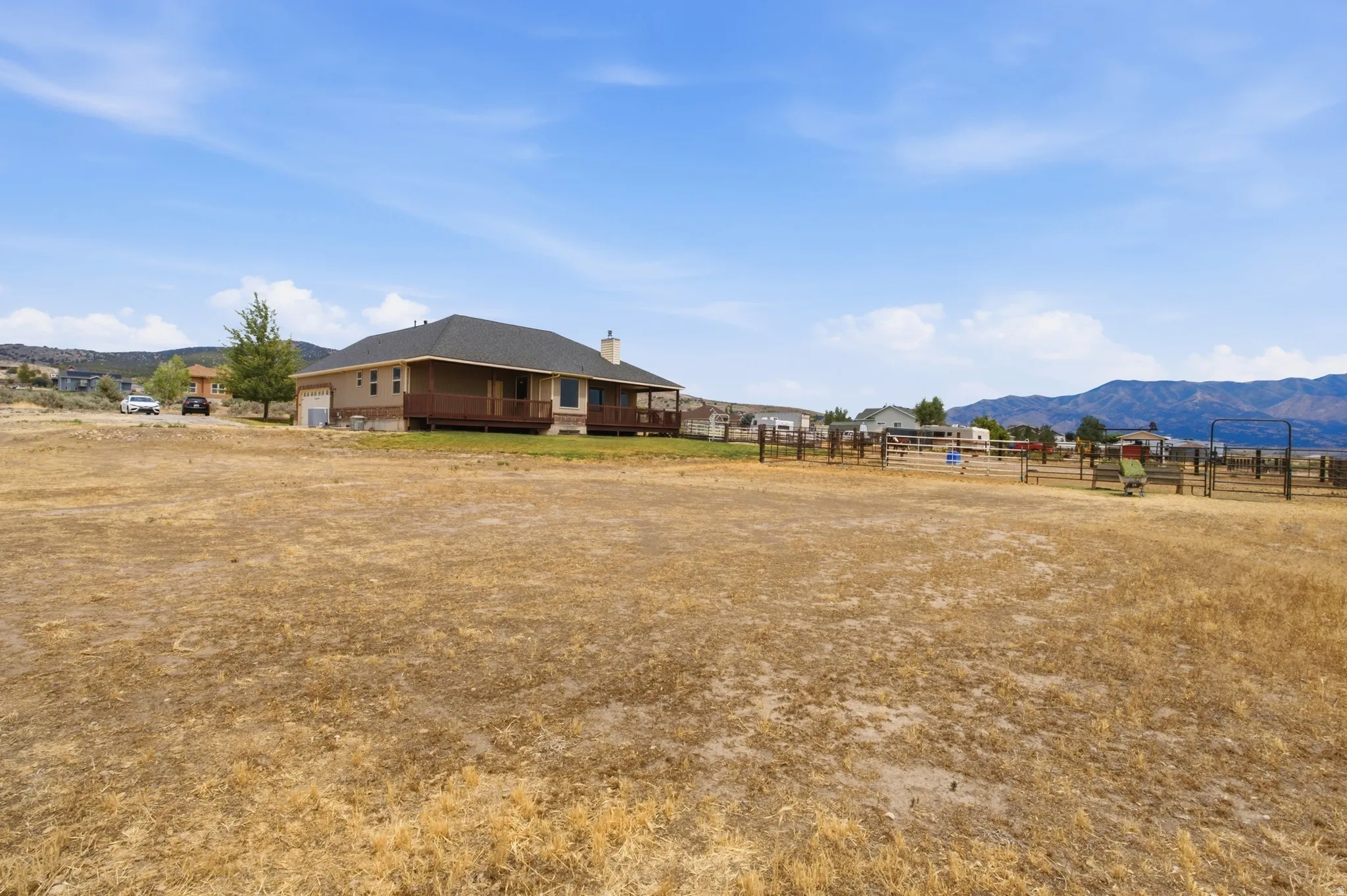 Expansive land parcel featuring a ranch-style home with a dark shingle roof and a full-length wooden deck