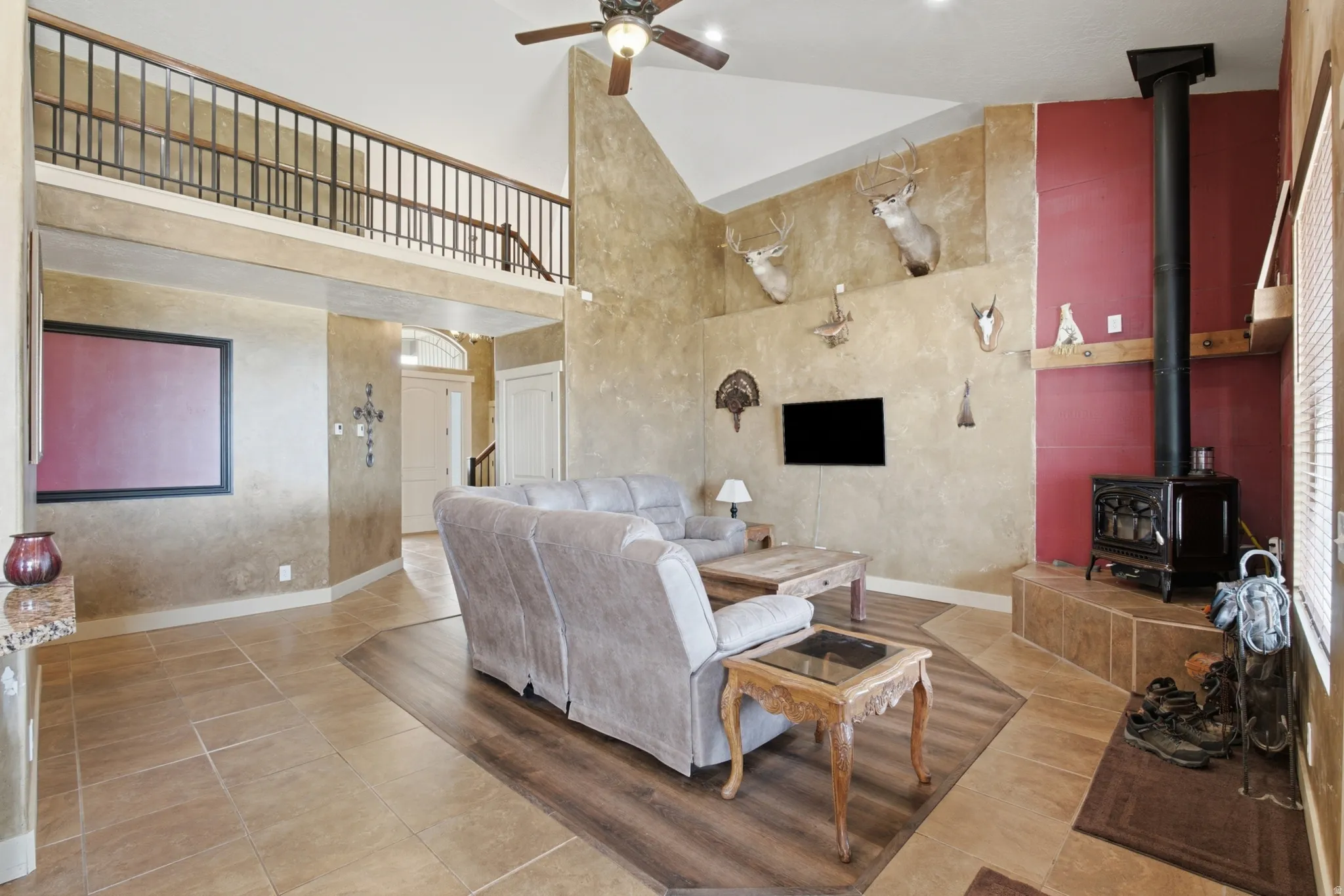 Vaulted living space with a loft, featuring a corner wood-burning stove on a tiled hearth, mixed flooring with large format tiles and wood-finish planks, and a ceiling fan