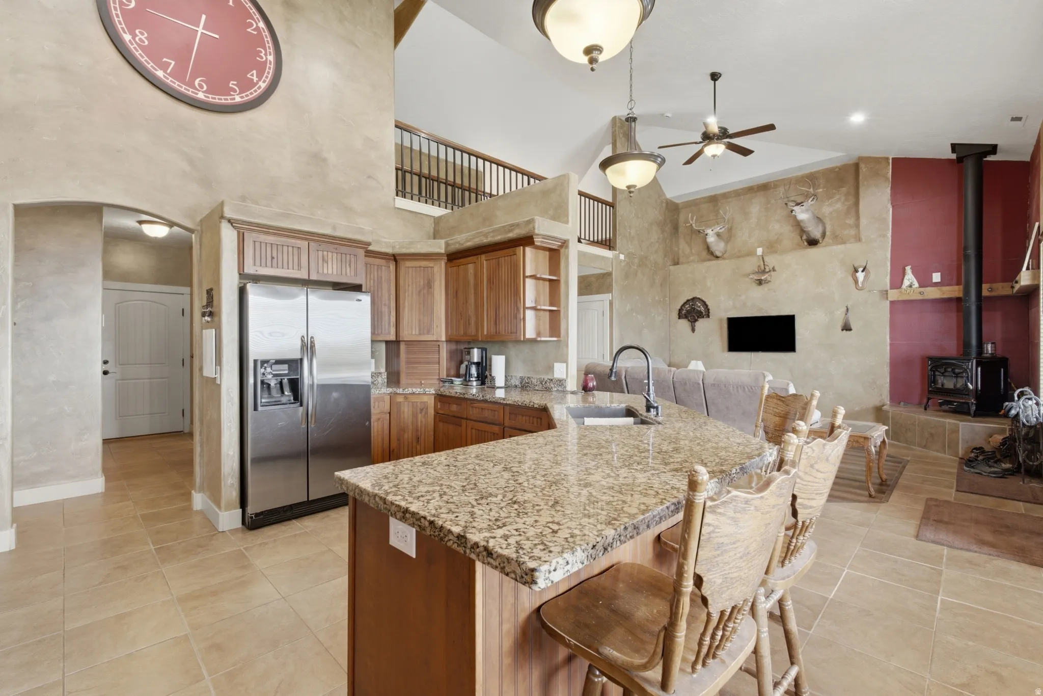 Kitchen featuring a granite countertop island with integrated sink, wood cabinetry, stainless steel refrigerator, and tiled flooring
