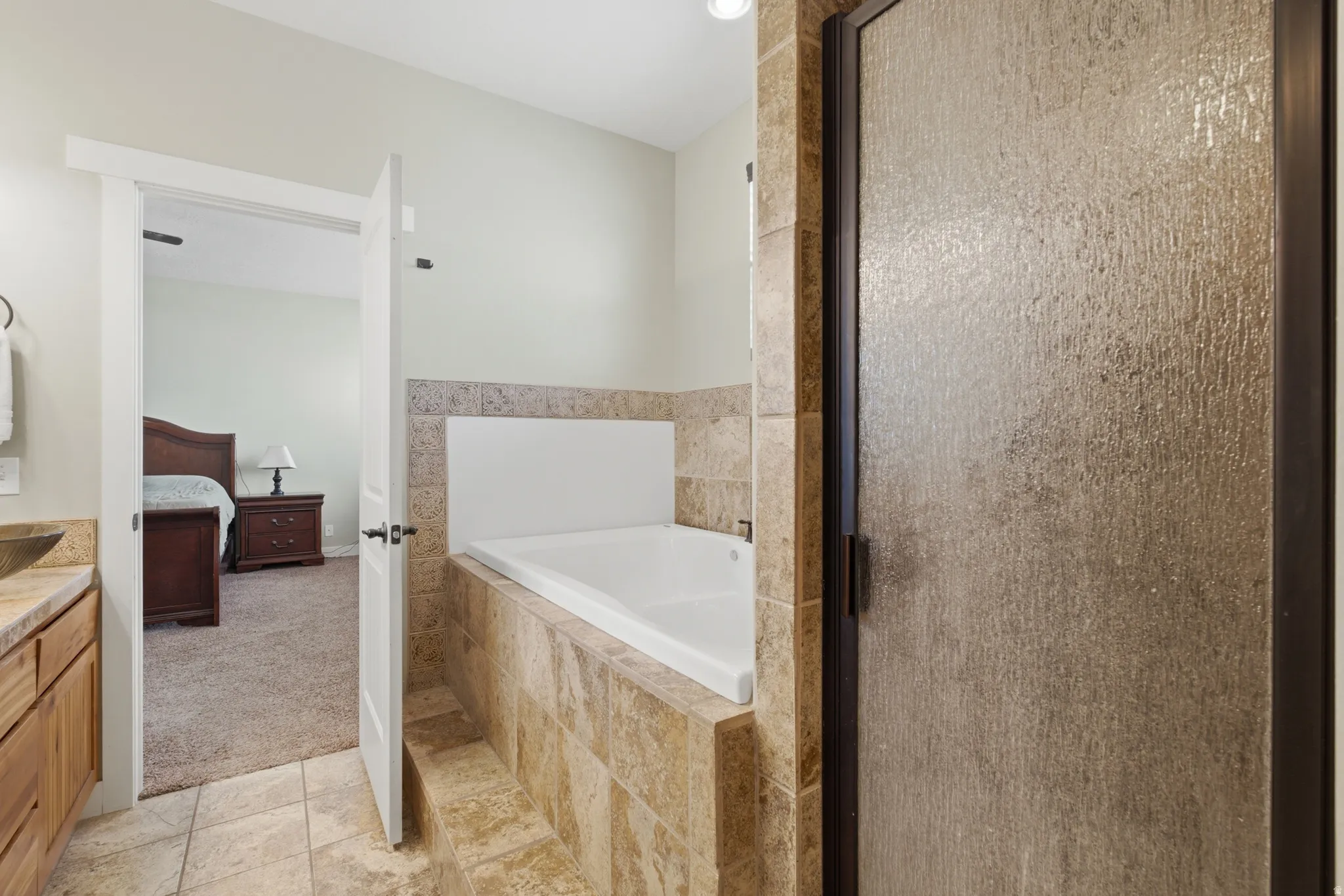 Tiled shower with obscure glass door, integrated built-in bathtub, natural stone tile surround, and coordinating floor tiles