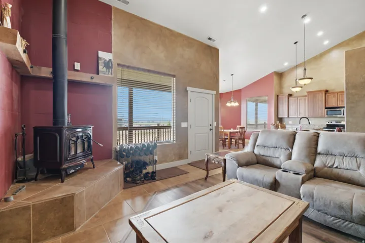 Living area featuring a freestanding stove on a tiled hearth, high ceilings, wood-finish flooring, and a large window with horizontal blinds