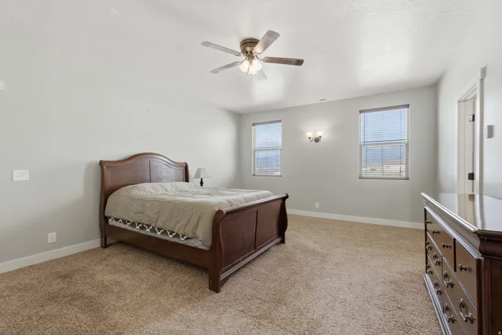 Carpeted room featuring light gray walls, two windows with horizontal blinds, a ceiling fan with integrated lighting, and a wall-mounted light fixture